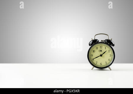 Vintage style metal alarm clock with bells standing on a white counter against a graduated grey background with central highlight and plenty of copysp Stock Photo