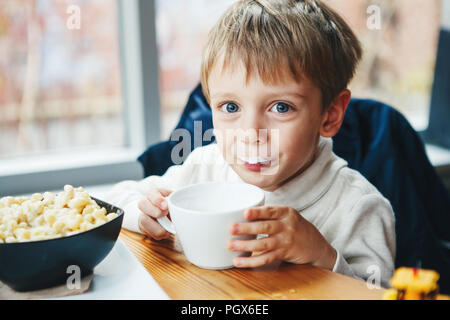 Portrait of cute adorable Caucasian child kid boy drinking milk from white cup eating breakfast lunch early morning, everyday lifestyle candid moments Stock Photo