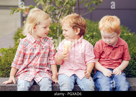 Group portrait of three white Caucasian cute adorable funny children toddlers sitting together sharing ice-cream food. Love friendship jealousy concep Stock Photo