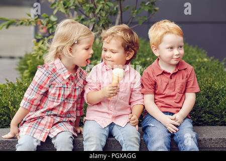 Group portrait of three white Caucasian cute adorable funny children toddlers sitting together sharing ice-cream food. Love friendship jealousy concep Stock Photo