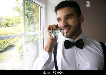 Smiling Professional business man, ceo in tuxedo talks on mobile cell phone by window Stock Photo