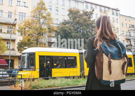 A tourist girl with a backpack on Berlin street crosses the road to the trom stop to continue her journey. Stock Photo