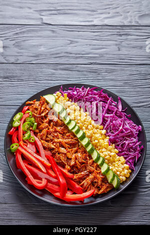 pulled pork rancho salad with coleslaw, corn, sweet pepper, cucumber and jalapeno on a black plate on a wooden table, vertical view from above Stock Photo