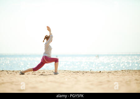 Side view of active female doing exercises for leg stretch and arms by waterside Stock Photo