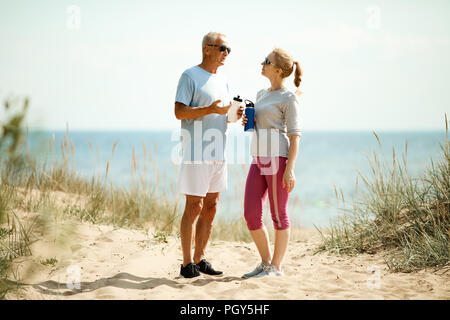 Couple of retired man and woman having water and discussing their success in morning trainings Stock Photo