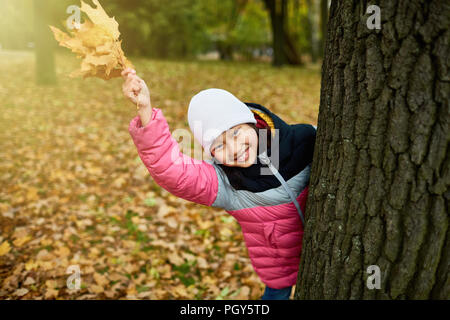 Cheerful youngster in warm clothes waving her hand with bunch of yellow maple leaves Stock Photo