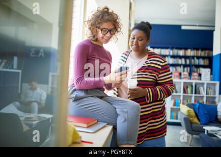Female college students using smart phone during break at college library Stock Photo