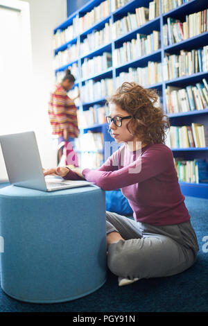 Serious female student  using laptop in school library using social media and studying Stock Photo
