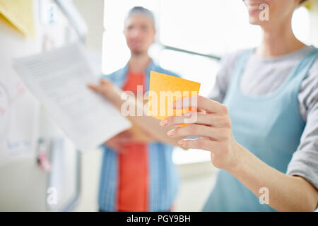 Close-up of positive manager holding adhesive note while planning project development with colleague and presenting her idea at meeting Stock Photo