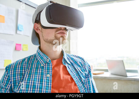 Serious student with beard wearing VR headset watching educational video and sitting in modern office Stock Photo