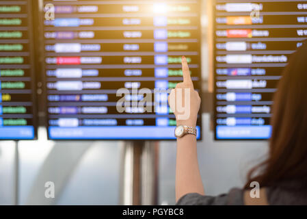 Back view of woman looking for flights from flight schedule in airport. Female tourist pointing at time table for take off plane. Travel and transport Stock Photo