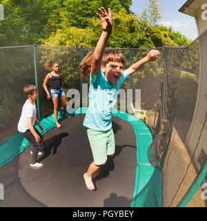 Portrait of excited boy jumping on the outdoor trampoline with his friends in summer Stock Photo
