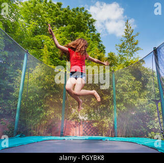 Portrait of active teenage girl jumping on trampoline with safety net outdoors
