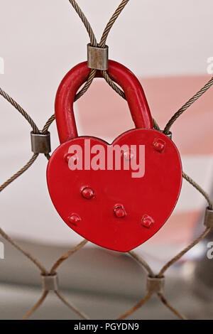 Close up view of red heart shape padlock hanging on fence. Concept of fidelity and infinite love Stock Photo