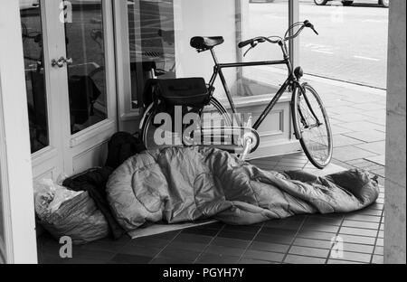 Black and white image of homeless person asleep in shop doorway Stock Photo