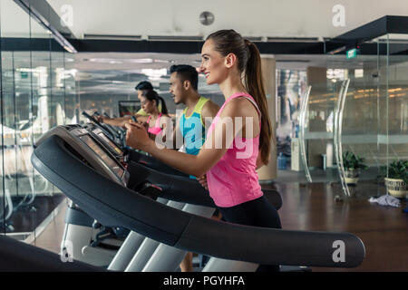 Cheerful beautiful woman with a healthy lifestyle drinking water during training on treadmill in a trendy fitness club Stock Photo