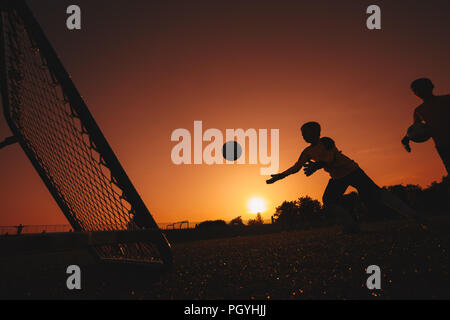 Football Soccer Goalkeeper Training Session. Two Young Goalies Practising in a Field. Soccer Equipment and Ball in the Foreground. Sunset Stock Photo