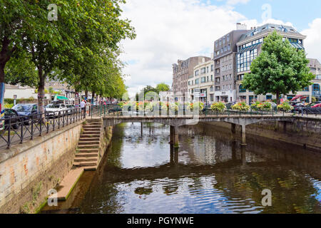 Quimper, France - August 8 2018: Looking down the Odet River flowing through Quimper, people walk on tree lined banks, bordered by commercial building Stock Photo