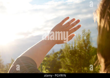 A young woman protects her eyes and skin from the sun with her hands. Sunlight, outdoor. Stock Photo