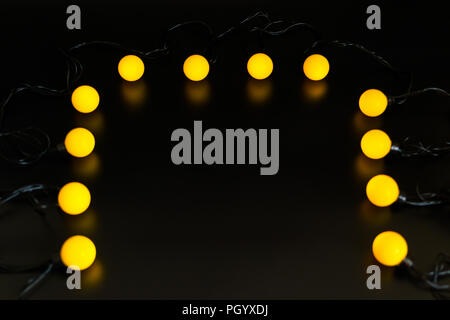 yellow glowing garland neatly straight-lined balls on a black background with light reflection Stock Photo