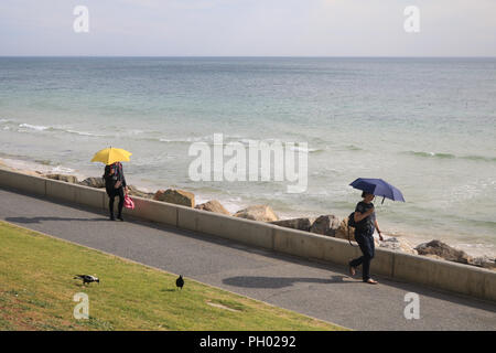 Adelaide Australia. 29 August 2018. People walking along the coast in Glenelg sheltering under umbrellas from the sun  on a warm sunny afternoon. Adelaide is experiencing warmer temperatures  on the final stages of the Australian winter season and the onset of spring Credit: amer ghazzal/Alamy Live News Stock Photo