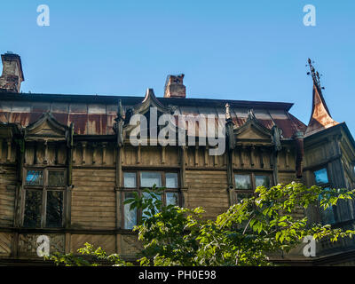 The facade of the wooden house in eclectic style with a bay window, carved attic windows, figured platbands, with a galvanized rusty roof on a clear s Stock Photo