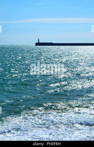 The Newhaven lighthouse and harbour wall are in the middle with a blue sunlit sea in the foreground and blue and white clouds in the background vertic Stock Photo