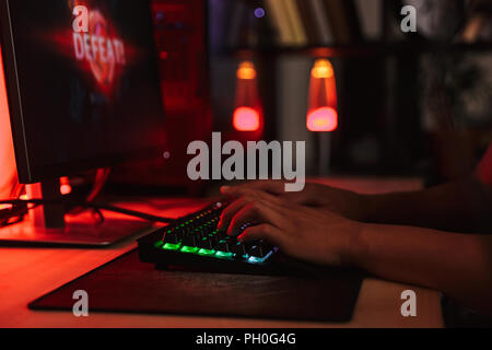 Hands of young gamer man playing video games on computer in dark room using backlit colorful keyboard Stock Photo