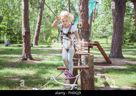 Child in forest adventure park. Kids climb on rope trail. Stock Photo