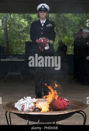 BANGOR, Wash. (June 14, 2018) Chief Hospital Corpsman Farrah Ocasio, from Detroit, Michigan, assigned to Trident Training Facility in Bangor, Wash., walks the remains of a U.S. flag to a fire during a flag retirement ceremony at Naval Base Kitsap - Bangor. When a U.S. flag becomes worn, torn, faded, or badly soiled, the flag should be retired with the dignity and respect befitting it. The traditional method is to cut the flag into pieces, separating the 13 stripes from canton and incinerating them separately in a respectful manner. Stock Photo