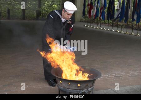 BANGOR, Wash. (June 14, 2018) Machinery Repairman 1st Class David Sams, from East Haddam, Connecticut, assigned to Trident Training Facility in Bangor, Wash., places the remains of a U.S. flag to a fire during a flag retirement ceremony at Naval Base Kitsap-Bangor. When a U.S. flag becomes worn, torn, faded, or badly soiled, it should be retired with the dignity and respect befitting it. BANGOR, Wash. (June 14, 2018) Musician 1st Class Chris Hodges, from Tuscaloosa, Alabama, assigned to Navy Band Northwest, plays the trumpet during a flag retirement ceremony at Naval Base Kitsap - Bangor. When Stock Photo