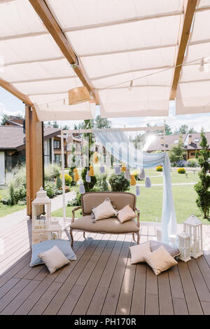 Cozy zone for a photoshoot on a terrace. A beautiful soft sofa, white wooden lamps and tassels made of thread Stock Photo