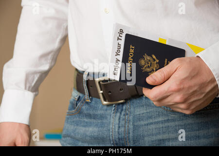 Image of a persons hand holding American passport and ready to travel. Man in a white shirt and jeans holding U.S. passport. Stock Photo