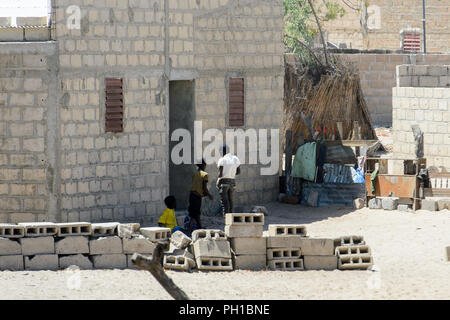 ROAD TO LAMPOUL, SENEGAL - APR 23, 2017: Unidentified Senegalese three little boys stand behind the wall from bricks. Still many people in Senegal liv Stock Photo