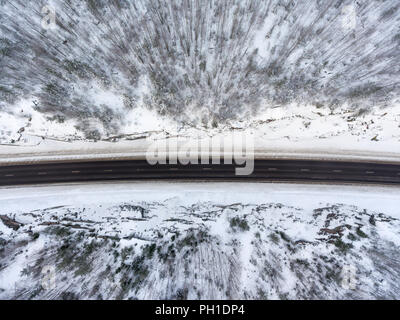 Top view at wintry slippery highway passing through snow covered coniferous forests in mountains Stock Photo