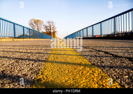 Part of the bridge structure at close. In the center of the frame is yellow roadsign tape, you can see the texture of the asphalt and shade from the s Stock Photo