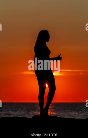 A woman gives a 'thumbs up' while silhouetted at sunset on the jetty at Menemsha Beach in Chilmark, Massachusetts on Martha's Vineyard.