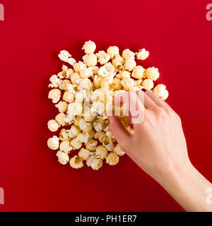 popcorn on red background, female hand takes, top view Stock Photo