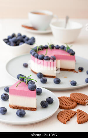 The two-color blueberry mini cheese cake. Round no bake cheesecake, cut portion on small plate with few cookies in the focus. The top of cake decorate Stock Photo