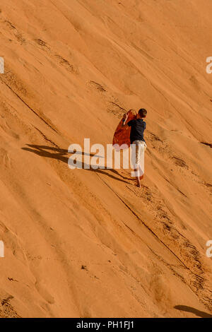 LAMPOUL DESERT, SENEGAL - APR 23, 2017: Unidentified tourist's little boy walks with the board to the top of sand dune in a Lampoul Desert, beautiful  Stock Photo