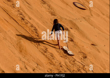 LAMPOUL DESERT, SENEGAL - APR 23, 2017: Unidentified tourist's little girl walks with the board to the top of sand dune in a Lampoul Desert, beautiful Stock Photo