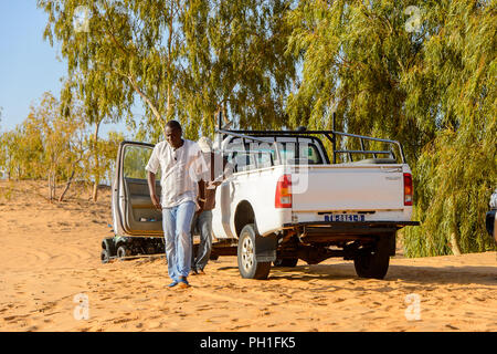 LAMPOUL DESERT, SENEGAL - APR 23, 2017: Unidentified Senegalese man walks near the car in a Lampoul Desert, beautiful landscape place Stock Photo