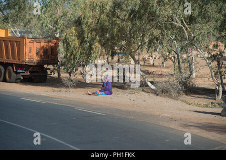 LAMPOUL DESERT, SENEGAL - APR 23, 2017: Unidentified Senegalese woman sits on the ground beside the road near the truck in a village near the Lampoul  Stock Photo