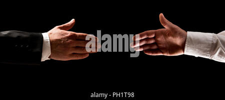 Two men reaching out to shake hands, one in a suit and the other in his shirtsleeves over a dark background. Stock Photo
