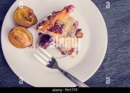 Top view of home baked plum pie served on a plate for dessert with a halved fresh plum alongside. With retro filter effect. Stock Photo