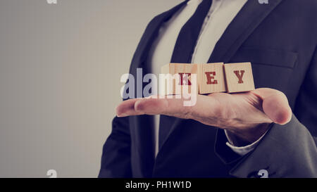 Retro style image of a businessman holding three wooden cubes displaying word Key. Stock Photo