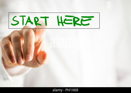 The phrase Start here on a virtual interface in a navigation bar with a businessman touching it with his finger from behind. Stock Photo