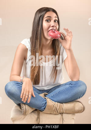 Pretty long-haired girl eating a donut sitting Indian style on a chair. Stock Photo