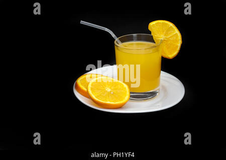 A glass of orange juice on a saucer next to slices of orange. Presented on a black background. Stock Photo
