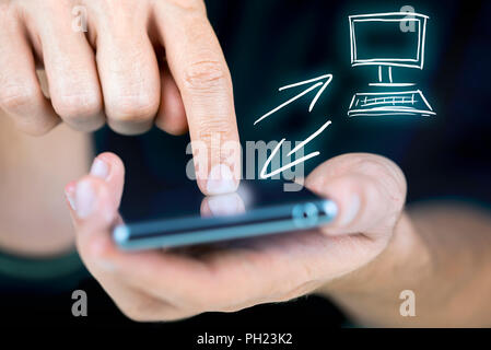 Man synchronizing his mobile and desktop in a conceptual image with a hand-drawn icon for the desktop, closeup view of his hands navigating the touch  Stock Photo
